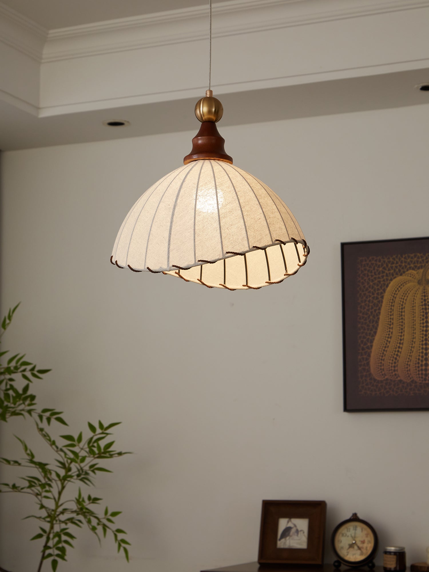 Suspension luminaire vintage en tissu plissé blanc, intérieur moderne, plante verte, horloge et cadre décoratif sur mur blanc.