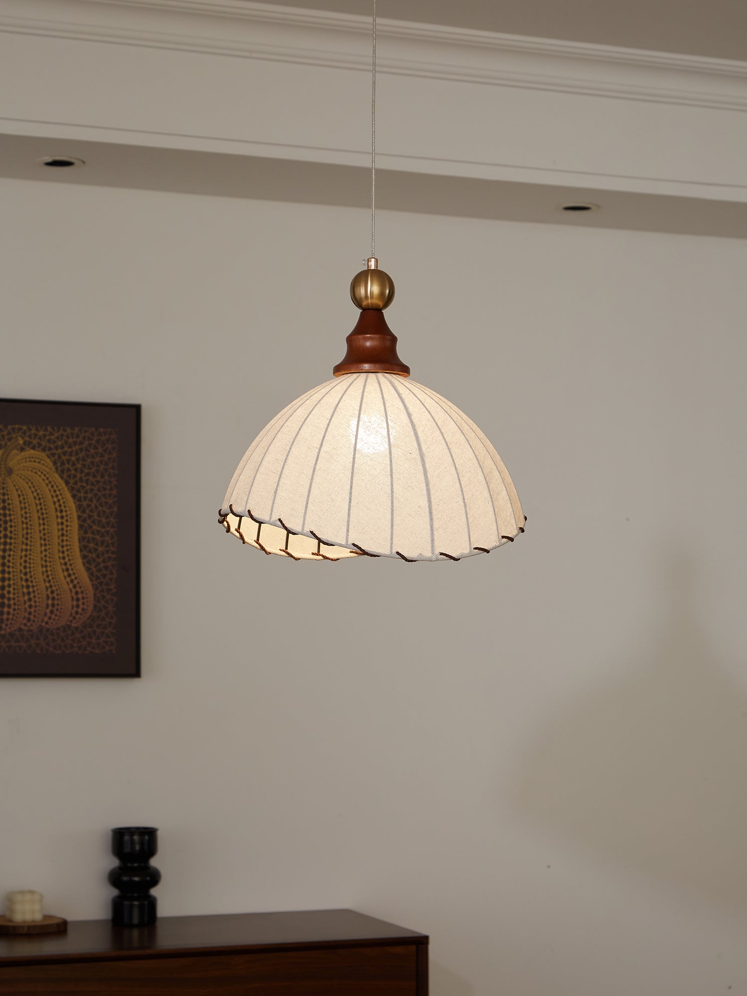 Suspension luminaire vintage avec abat-jour plissé blanc, intérieur moderne, mur blanc, tableau encadré, éclairage décoratif élégant.