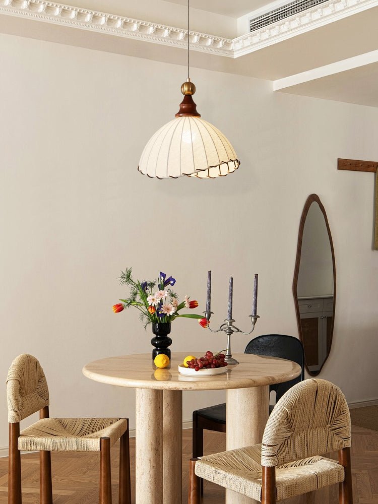 Salle à manger moderne avec table en marbre, chaises en rotin, suspension en tissu, vase de fleurs colorées, bougies et miroir ovale.
