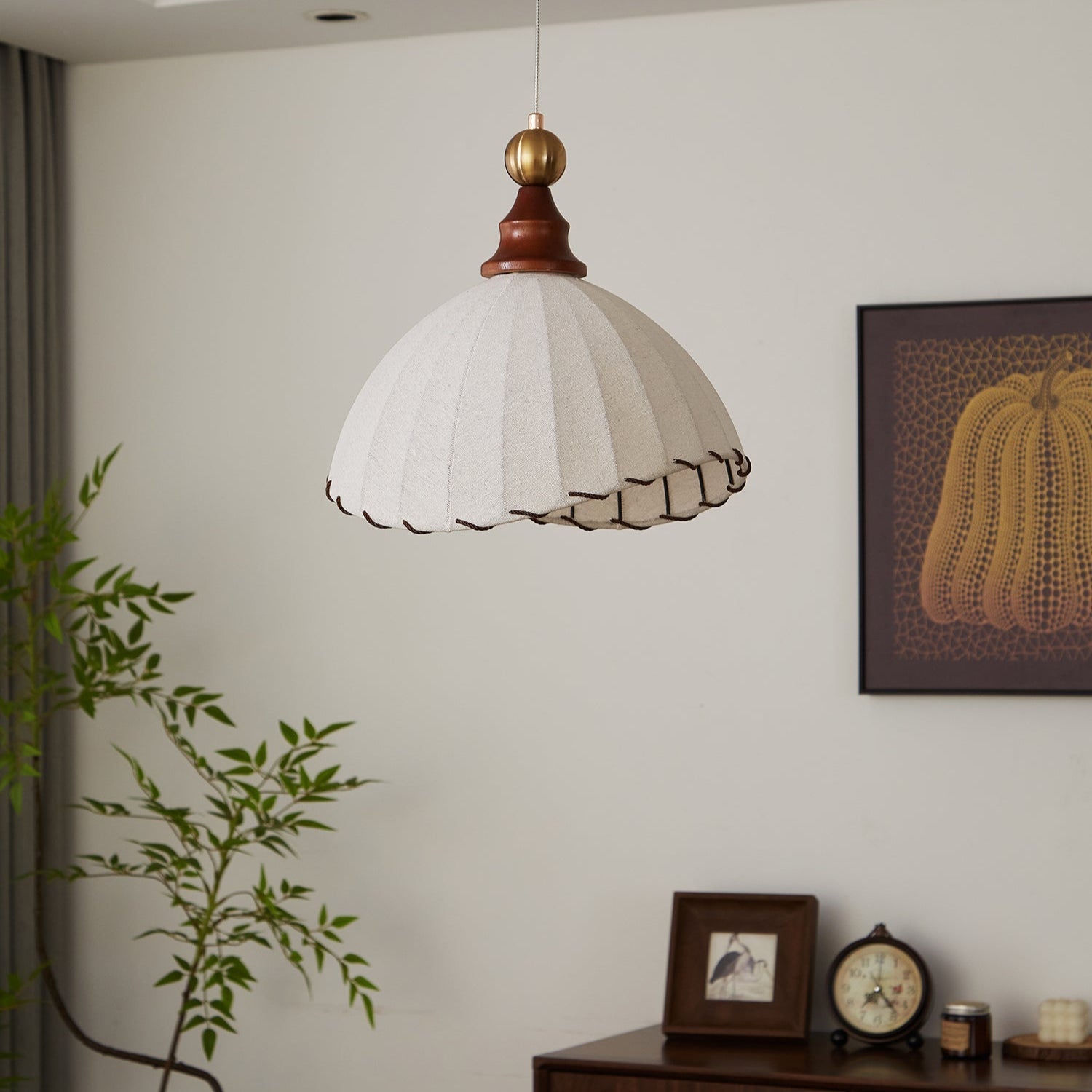 Suspension luminaire moderne en tissu blanc avec bordure marron, décor intérieur élégant, plante verte, horloge vintage, cadre photo, tableau mural.