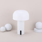 Lampe de table moderne blanche en forme de champignon, design minimaliste, posée sur une surface beige avec des sphères décoratives blanches.