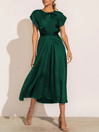 Robe longue verte élégante avec manches courtes, ceinture nouée à la taille, portée par une femme en talons beiges. Mode féminine chic et tendance.