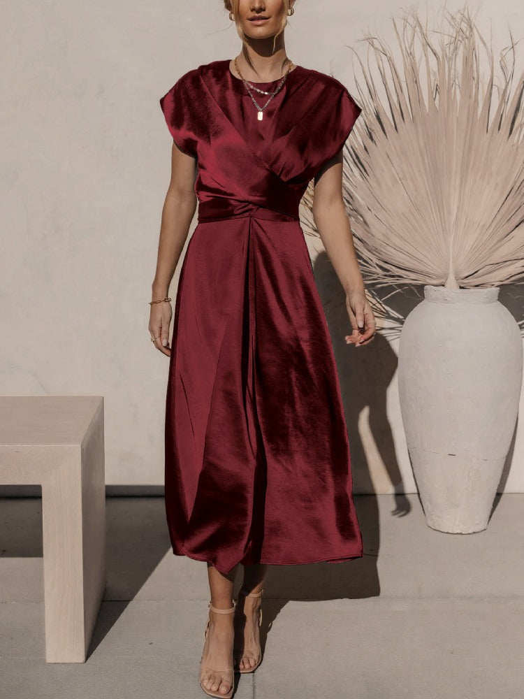 Robe midi rouge élégante en satin, femme debout devant un vase blanc moderne avec des plantes séchées, style chic et minimaliste.