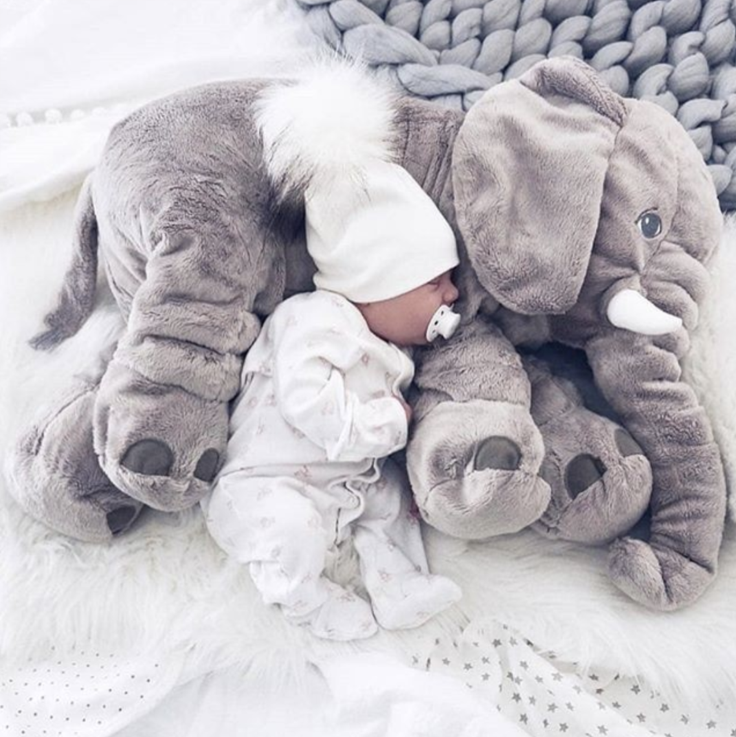 Bébé endormi avec une tétine, blotti contre une peluche éléphant grise sur un lit douillet, couverture tricotée en arrière-plan.