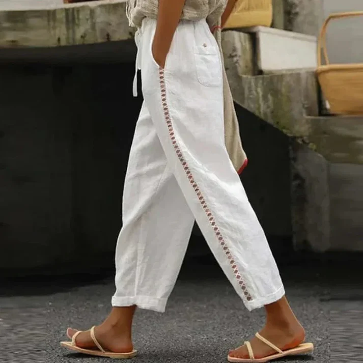 Pantalon blanc en lin avec détails brodés sur le côté, porté avec des sandales marron. Mode estivale décontractée pour femme.