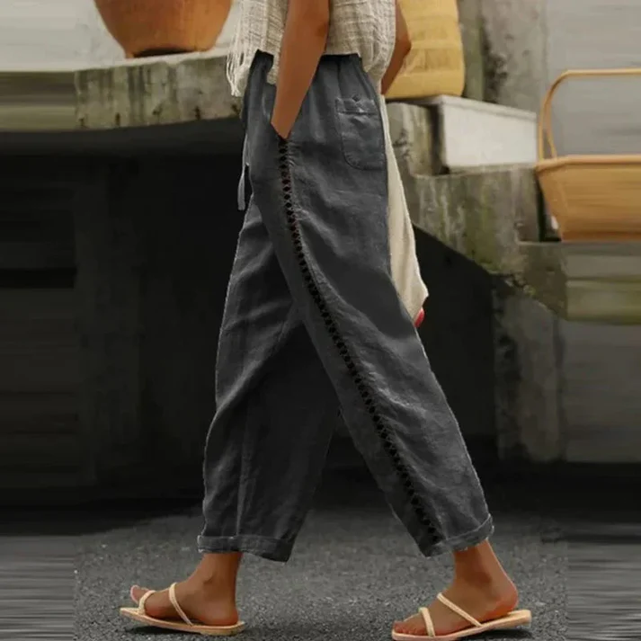 Pantalon ample en lin gris avec détails brodés, porté par une personne marchant en sandales blanches, style décontracté et estival.