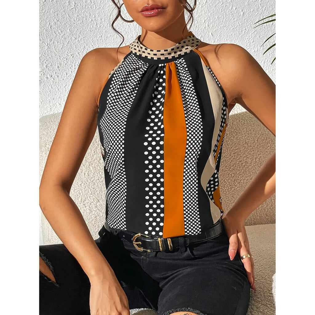 Femme portant un haut sans manches à motifs géométriques noir, blanc et orange, assise sur un canapé beige, style moderne et chic.