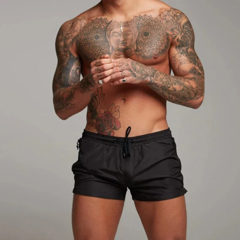 Homme musclé torse nu avec tatouages complexes, portant un short noir. Tatouage Bouddha sur le torse. Mode masculine, style tatouage.