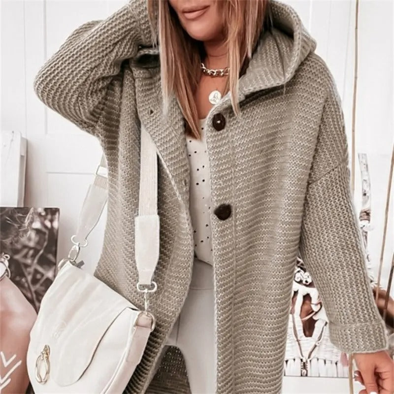 Femme portant un manteau en tricot gris avec capuche, sac à main blanc, collier doré, tenue décontractée chic, mode automne-hiver tendance.
