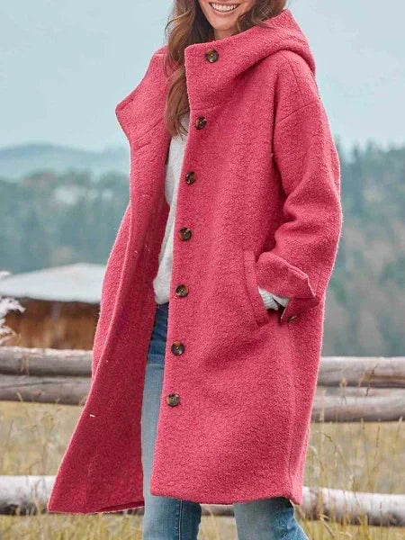 Femme portant un manteau rose en laine bouclée avec boutons, paysage rural en arrière-plan. Mode automne-hiver, style décontracté et élégant.