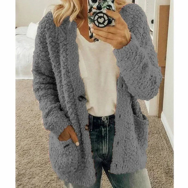 Femme portant un cardigan en laine gris, tenant un smartphone. Mode automne-hiver, tenue décontractée avec jean et t-shirt blanc.