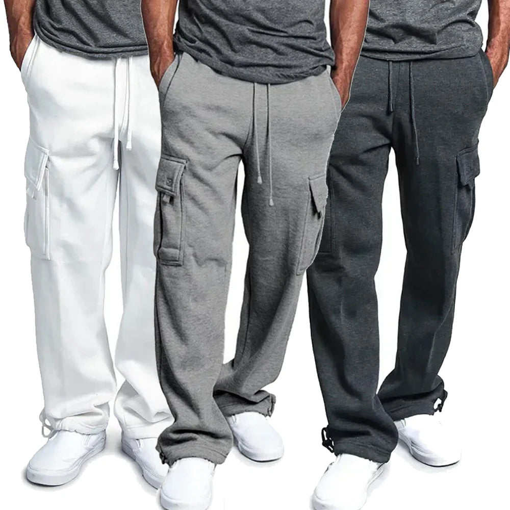 Trois pantalons de jogging pour homme en coton, couleurs blanc, gris clair et gris foncé, avec poches cargo, portés avec des baskets blanches.
