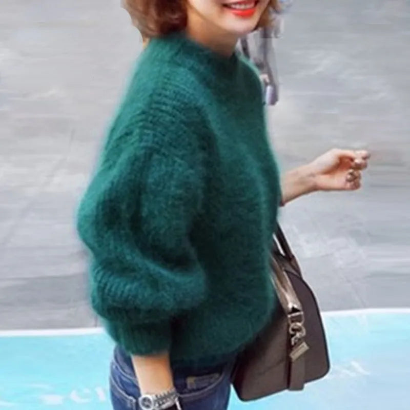 Femme portant un pull vert en laine, manches longues, avec un sac à main marron. Mode automne-hiver, style décontracté et élégant.