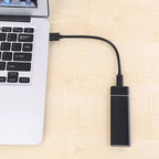 Ordinateur portable connecté à un disque dur externe noir via un câble USB, posé sur un bureau en bois clair. Stockage de données portable.