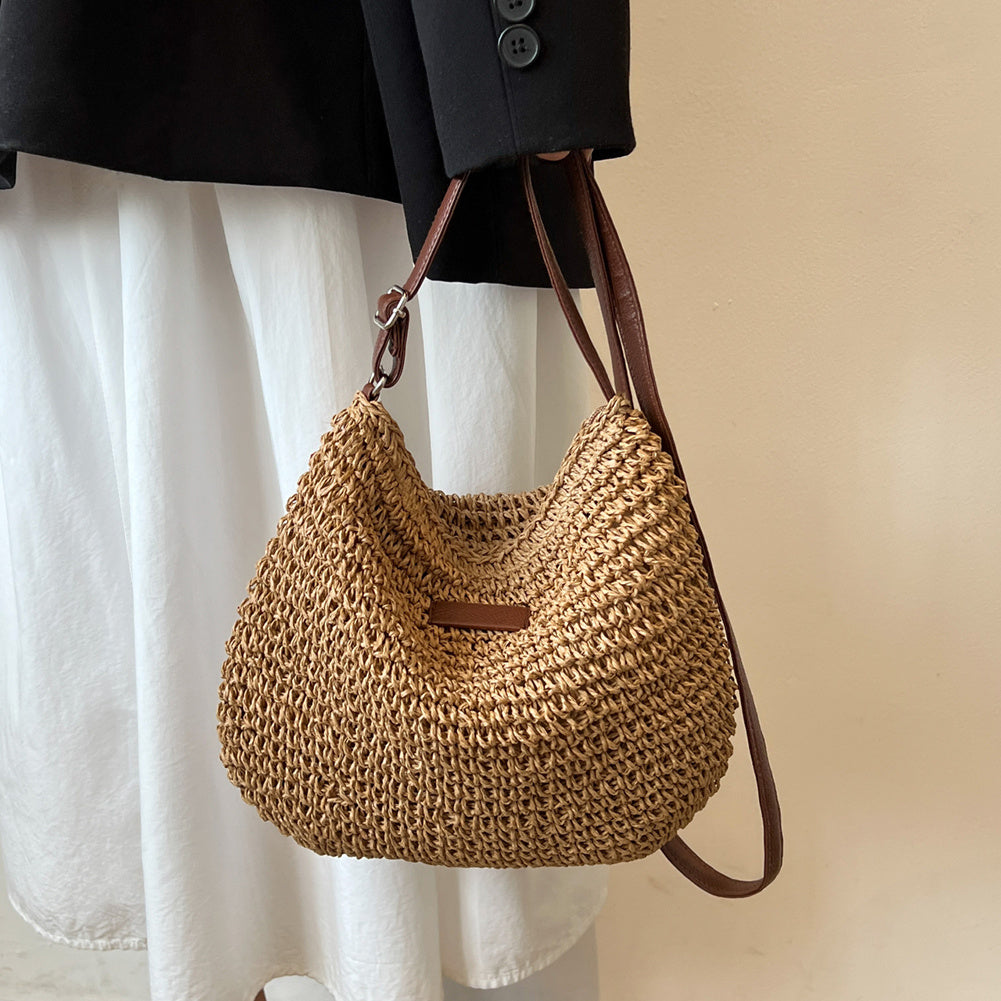 Sac à main en paille tressée beige avec bandoulière marron, porté par une personne en jupe blanche et veste noire. Mode, accessoire, tendance.