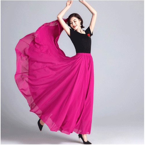 Femme dansant en robe longue rose vif, bras levés, fond gris. Mode élégante, mouvement fluide, style moderne.