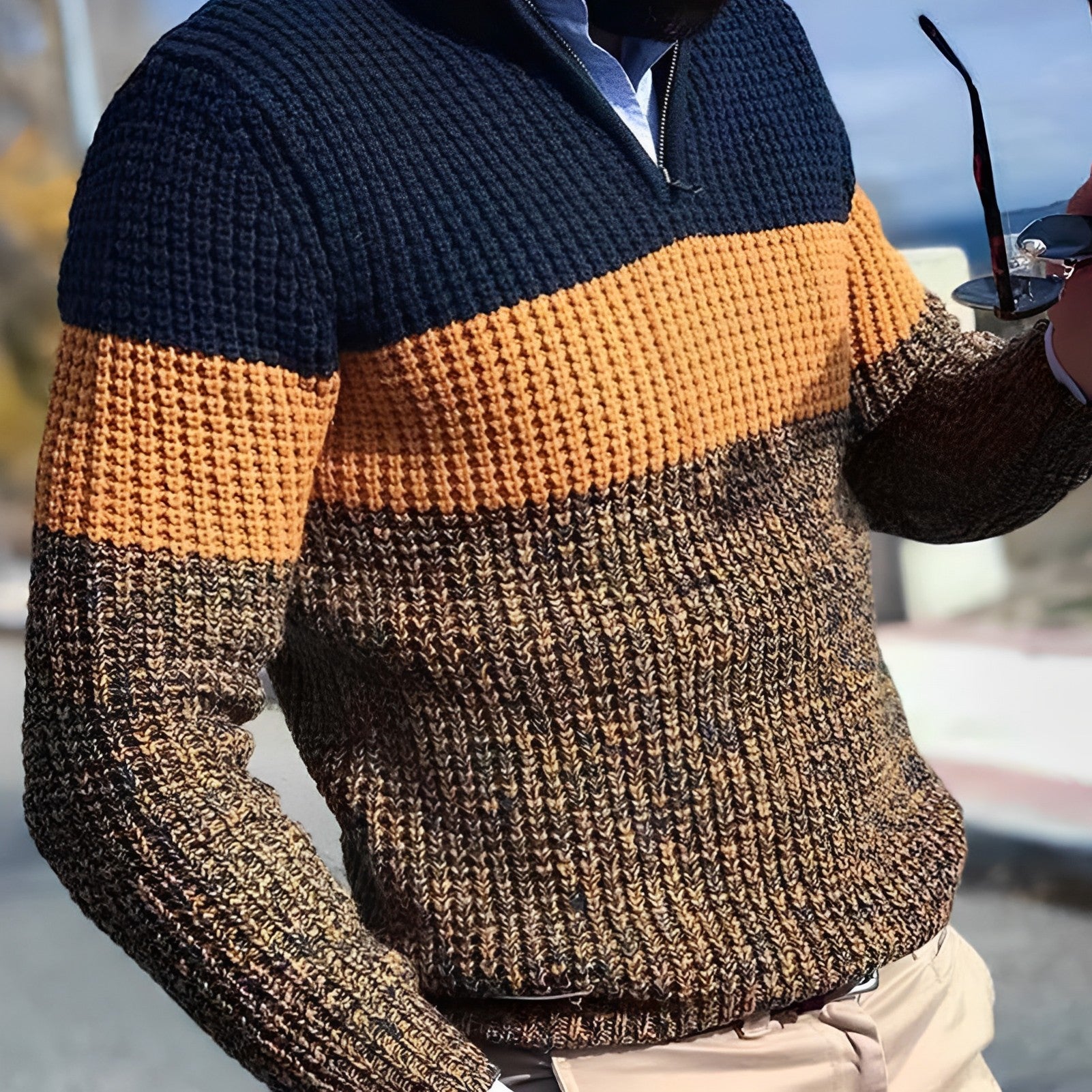 Pull homme en maille épaisse, rayé bleu marine, orange et marron, porté avec chemise bleue. Mode automne-hiver, style décontracté élégant.