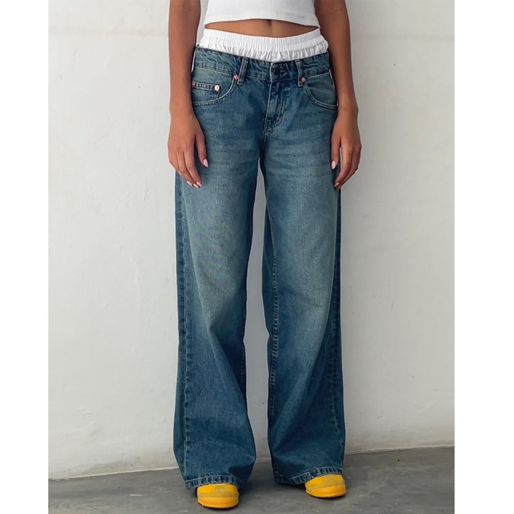 Jeune femme portant un jean large bleu taille haute, avec un haut blanc court et des baskets jaunes. Mode décontractée, tendance streetwear.