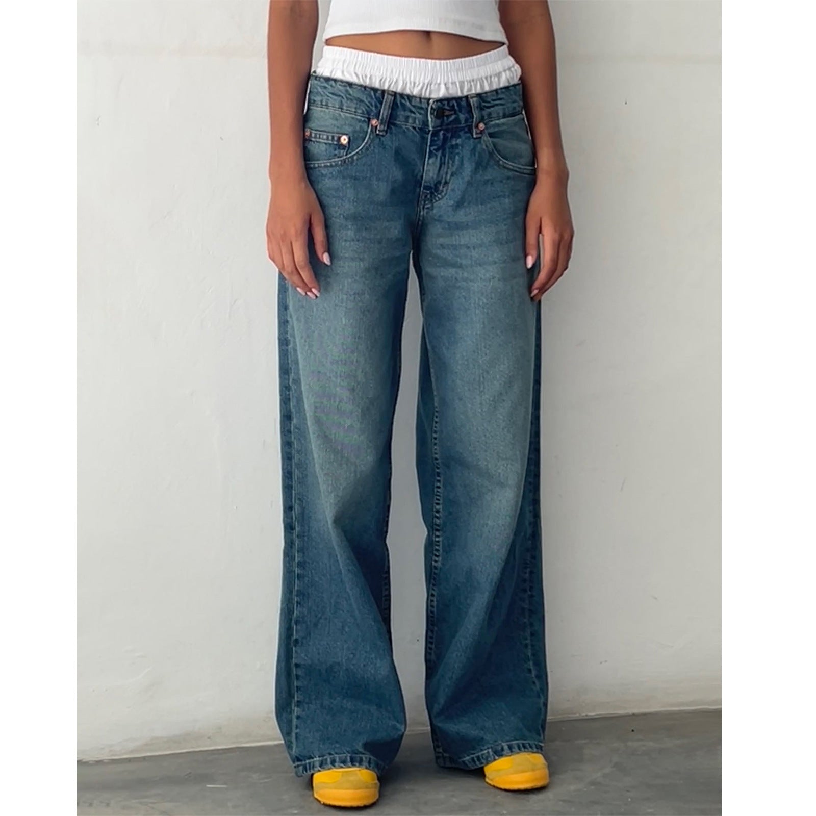 Jeune femme portant un jean large bleu taille haute, avec un haut blanc court et des baskets jaunes. Mode décontractée, tendance streetwear.