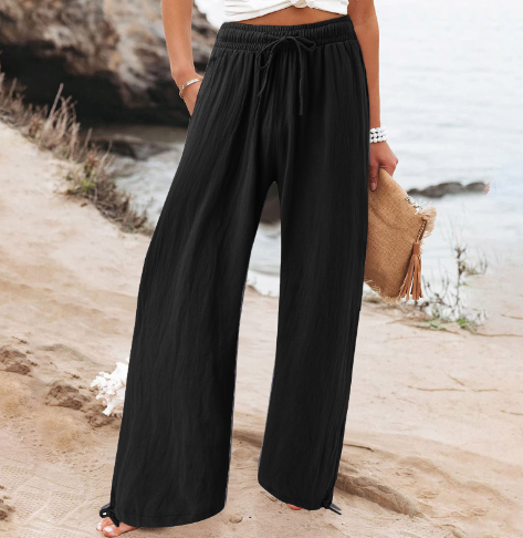 Pantalon large noir femme, taille haute, plage en arrière-plan, style décontracté, mode estivale, tenue confortable, bord de mer.