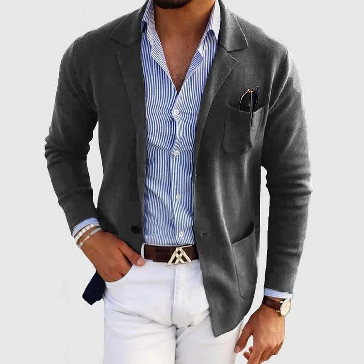 Homme élégant portant une veste grise, chemise rayée bleue et blanche, pantalon blanc; style mode masculine chic et moderne.
