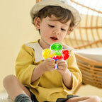 Enfant jouant avec un jouet pop it coloré, assis dans une chaise en rotin. Vêtements jaunes et chapeau beige. Activité ludique et sensorielle.