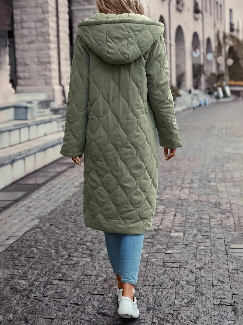 Femme portant un manteau long matelassé vert avec capuche, marchant sur un trottoir pavé. Mode hiver, style décontracté, vêtements chauds.