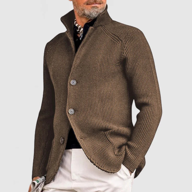 Veste en maille marron pour homme, élégante et moderne, avec boutons, col relevé, portée sur chemise noire et pantalon blanc. Mode masculine chic.