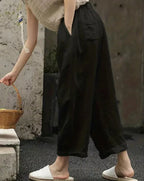 Pantalon large noir en lin pour femme, style décontracté, avec poches, porté avec des mules blanches. Mode estivale confortable et élégante.