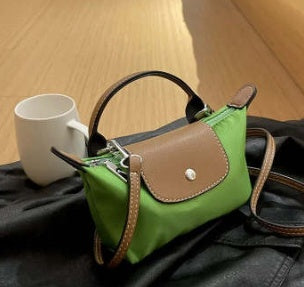 Petit sac à main vert avec rabat marron, posé sur une veste noire, à côté d'une tasse blanche. Accessoire mode élégant et tendance.