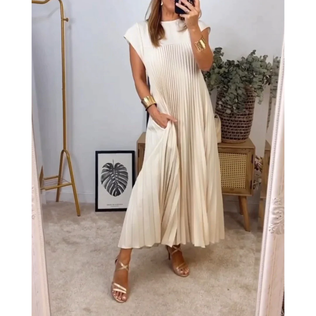 Robe plissée beige élégante portée par une femme, accessoires dorés, miroir, plante verte, cadre avec feuille, ambiance moderne et chic.
