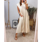 Robe plissée beige élégante portée par une femme, accessoires dorés, miroir, plante verte, cadre avec feuille, ambiance moderne et chic.