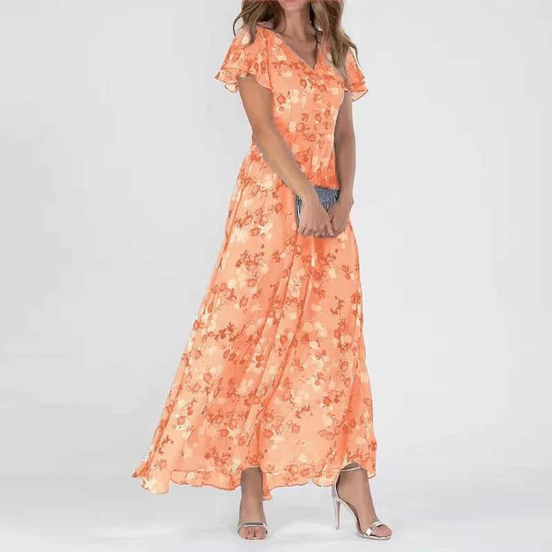 Robe longue orange à motifs floraux, manches courtes, portée par une femme avec des sandales argentées et une pochette grise. Mode féminine élégante.