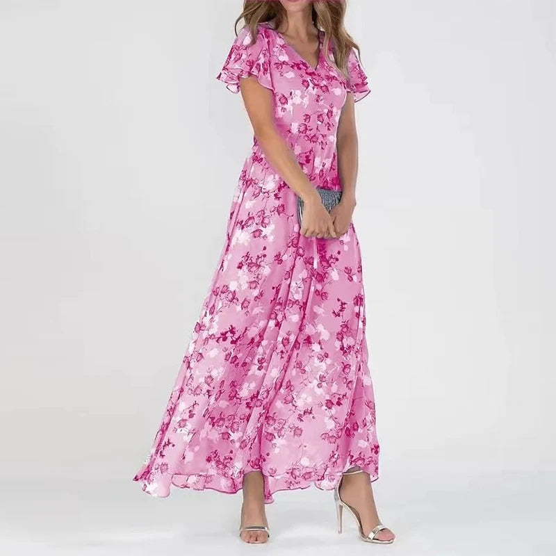 Robe longue rose à motifs floraux, manches courtes, portée par une femme, accessoirisée d'une pochette argentée et de sandales à talons.