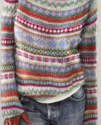 Pull en laine multicolore à motifs géométriques, rayures et fleurs, porté avec un jean décontracté. Mode automne-hiver, style bohème chic.
