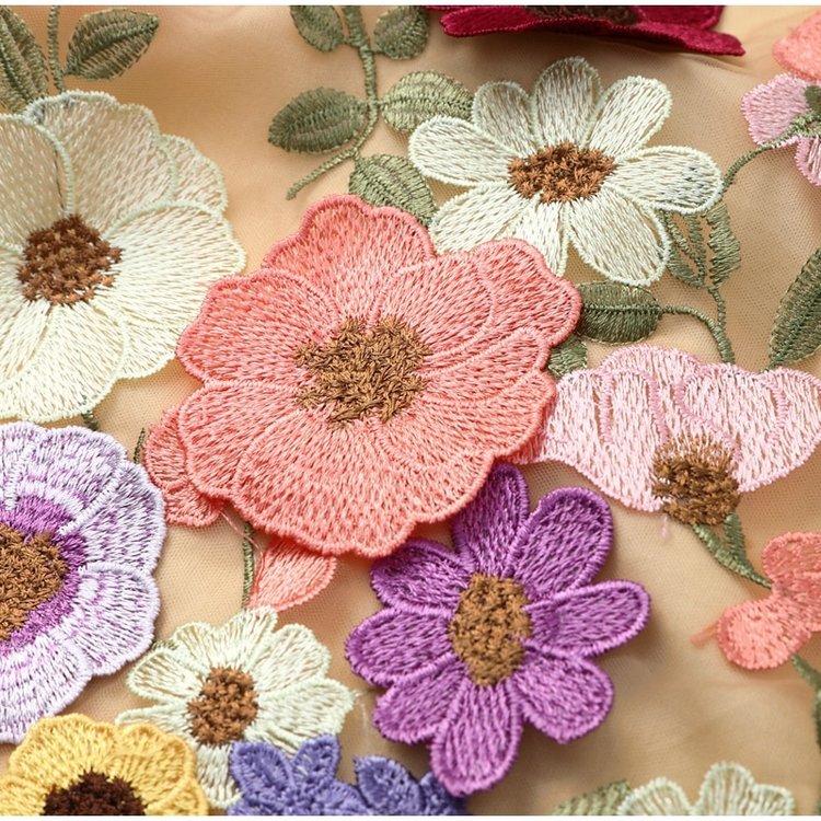 Broderie florale colorée sur tissu beige, avec fleurs roses, violettes et blanches. Motif détaillé et élégant, idéal pour la mode et la décoration.