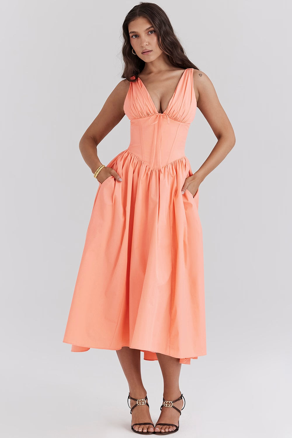 Robe midi orange pêche élégante, décolleté plongeant, sans manches, poches latérales, portée par une femme. Mode féminine chic et estivale.