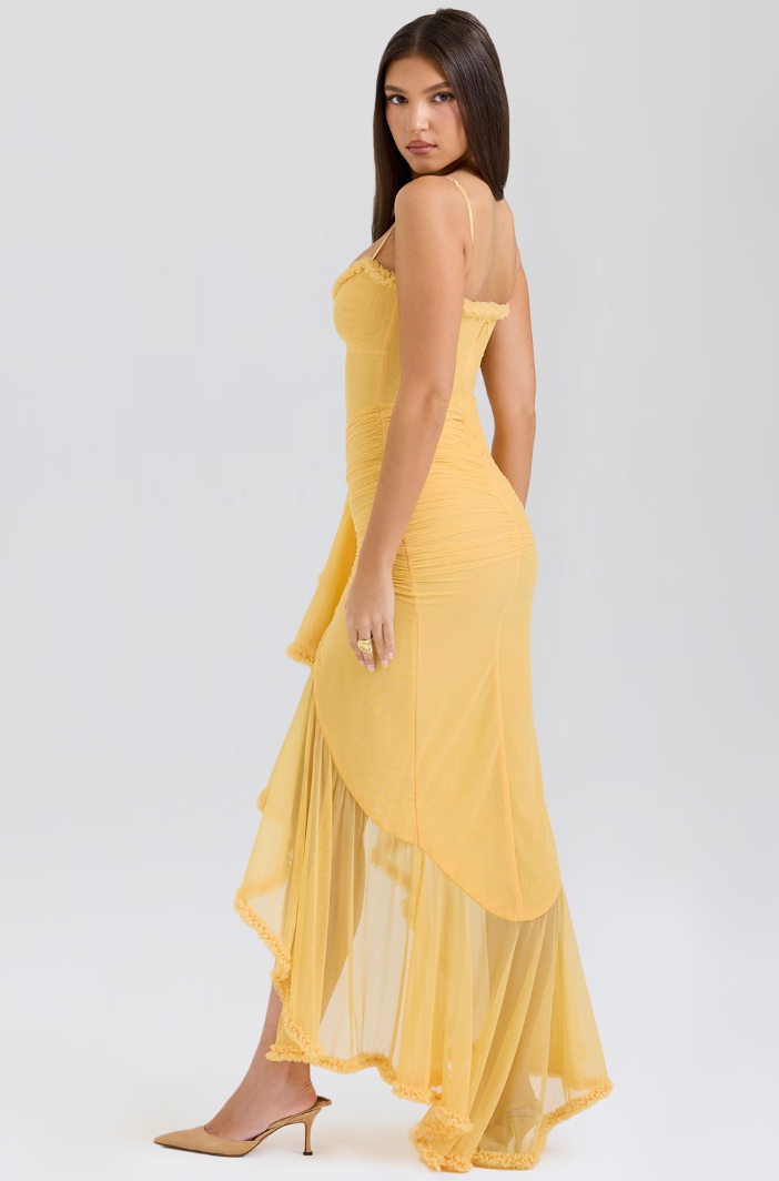 Robe longue jaune élégante en mousseline, avec bretelles fines et ourlet asymétrique, portée par une femme sur fond blanc. Mode féminine chic.