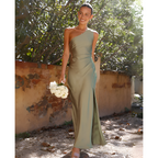 Une femme souriante en robe de soirée verte asymétrique, tenant un bouquet de fleurs blanches, marche dans un jardin ensoleillé.