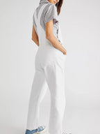 Femme portant une salopette blanche, chemise rayée et baskets bleues. Mode décontractée, style moderne, tenue estivale tendance.