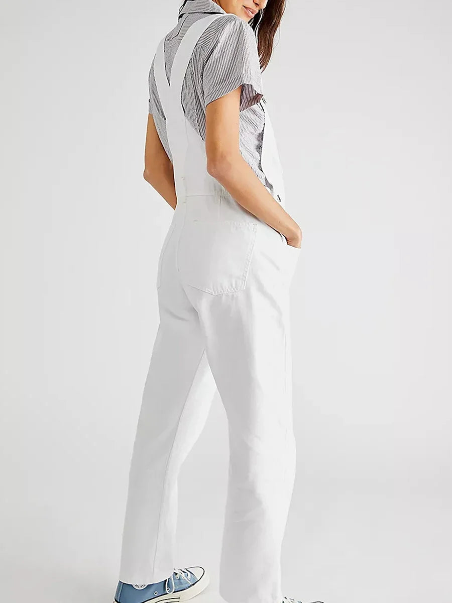 Femme portant une salopette blanche, chemise rayée et baskets bleues. Mode décontractée, style moderne, tenue estivale tendance.