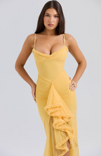 Femme en robe jaune élégante avec volants, posant sur fond neutre. Mode féminine, style glamour, tenue de soirée chic.