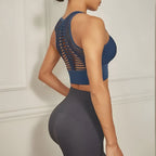 Femme en tenue de sport, portant un débardeur bleu à dos ajouré et un legging gris foncé, posant de dos dans un intérieur minimaliste.