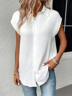 Femme portant une chemise blanche texturée à manches courtes, associée à un jean bleu clair. Style décontracté, mode féminine tendance.