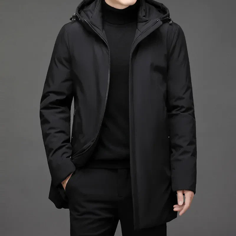 Homme portant un manteau noir élégant avec capuche, style moderne et minimaliste, sur fond gris. Mode masculine, vêtement d'hiver chic.