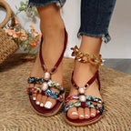 Sandales bohèmes à motifs floraux colorés, ornées de bijoux, portées avec un jean. Chaussures d'été tendance pour femmes sur tapis en jute.
