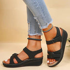Sandales compensées noires pour femme, portées avec un jean déchiré. Chaussures d'été élégantes, confortables, idéales pour un look décontracté.