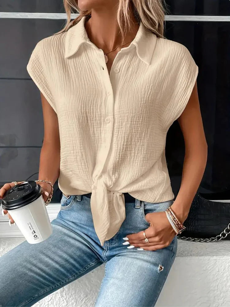 Femme portant une chemise beige nouée, manches courtes, avec un jean bleu déchiré. Elle tient un gobelet à café noir et blanc. Mode décontractée chic.