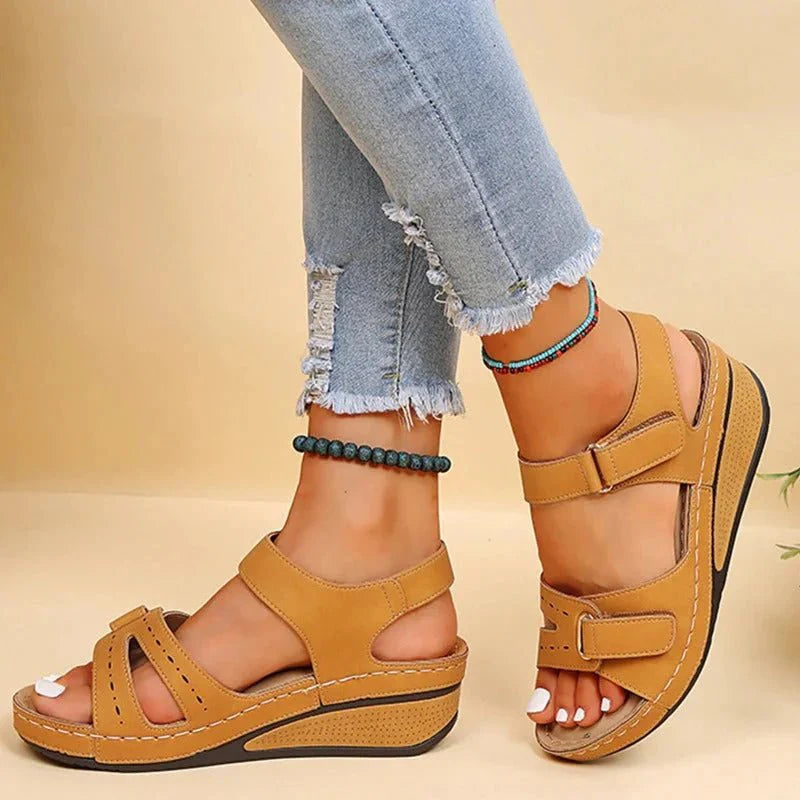 Sandales compensées marron en cuir, portées avec un jean déchiré et des bracelets de cheville colorés. Mode estivale, chaussures confortables pour femmes.