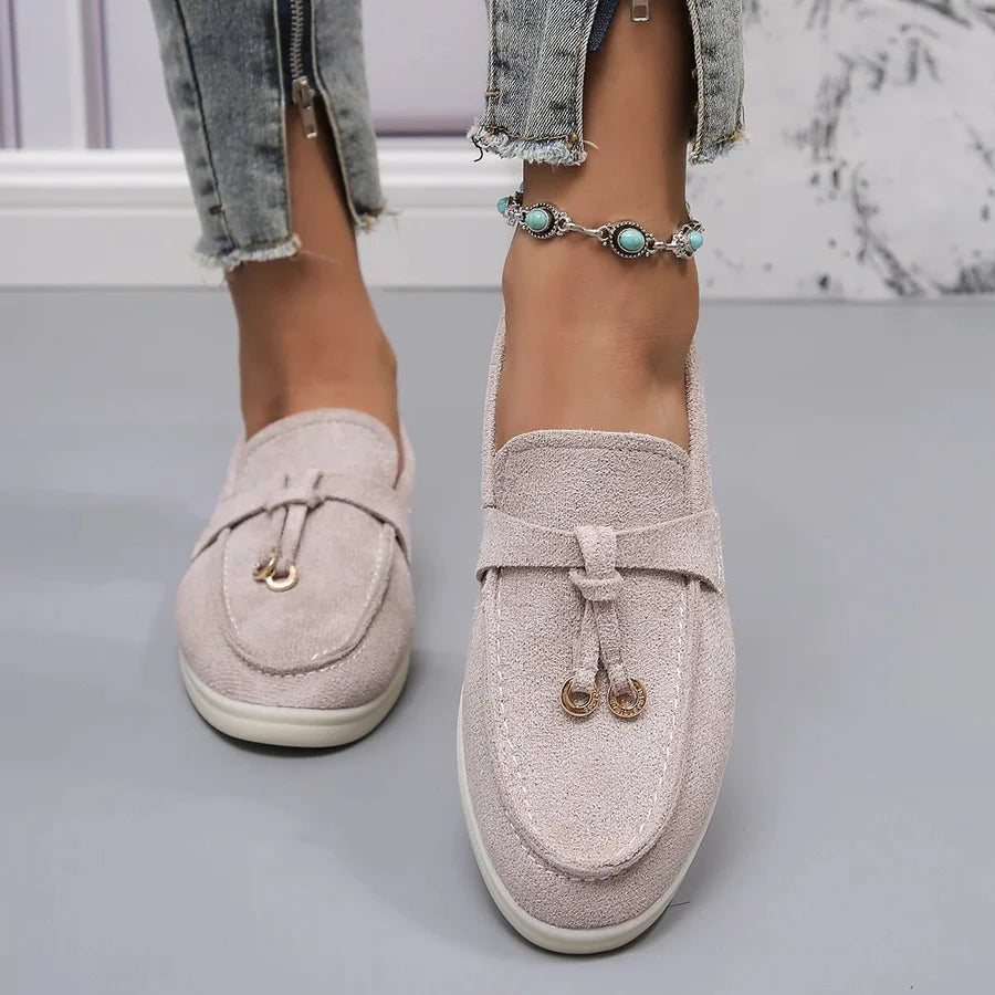 Chaussures mocassins beiges pour femme, en daim, avec boucle dorée, portées avec un jean déchiré et un bracelet de cheville turquoise.